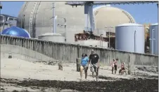  ?? AP PHOTO/LENNY IGNELZI ?? People walk on the sand near the shuttered San Onofre nuclear power plant in San Clemente, Calif., on June 30, 2011.