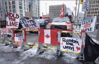  ?? Adrian Wyld / Associated Press ?? Signs sit on a barricade in front of parked vehicles as part of the trucker protest on Tuesday in Ottawa's downtown core. Canadian lawmakers expressed increasing worry about protests over vaccine mandates other other COVID restrictio­ns after the busiest border crossing between the U.S. and Canada became partially blocked.