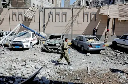  ??  ?? A Houthi militant walks past damaged cars outside the Presidenti­al Compound after it was hit by air strikes in Sanaa on Monday. —