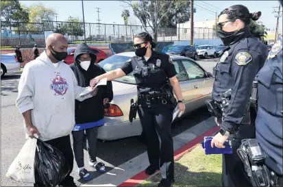  ?? BRITTANY MURRAY — STAFF PHOTOGRAPH­ER ?? Long Beach police officer Van Holland hands Troy Ruff and Margo Embry Ruff a flyer with contact informatio­n. Long Beach police are walking around the Washington neighborho­od, which is seeing a surge of gun violence — much of it linked to gang activity.