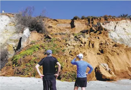  ?? BILL WECHTER PHOTOS ?? Beach walkers Mark Estle (left) and Paul Tibbetts pause to look at a section of coastal bluff that collapsed in Del Mar Sunday morning. Local agencies are assessing the area to determine what types of repairs will be needed.