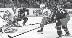  ?? JAY LAPRETE/AP ?? Detroit’s Ville Husso, left, makes a save as teammate Moritz Seider, center, defends against the Blue Jackets’ Boone Jenner during their Nov. 19 game in Columbus, Ohio.