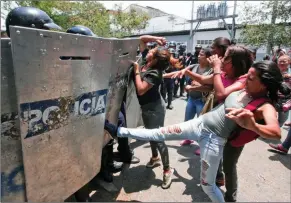  ?? ASSOCIATED PRESS ?? A WOMAN KICKS AT A RIOT POLICE SHIELD as relatives of prisoners wait to hear news about their family members imprisoned at a police station where a riot broke out, in Valencia, Venezuela, Wednesday. In a state police station housing more than one...