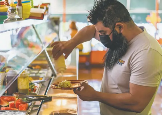  ?? Damian Dovarganes / Associated Press ?? Gustavo Arellano, 36, who is vaccinated, serves himself last week at Taqueria El Sol buffet in L.A. Masks are required for everyone indoors in Los Angeles County.