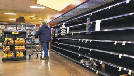  ?? MICHAEL CIAGLO GETTY IMAGES ?? A shopper walks past an empty bread section in a King Soopers grocery store Friday ahead of a winter storm in Golden, Colo. According to the National Weather Service, the storm is expected to bring 2 feet of snow to the Denver area and 2 to 4 feet of snow to the foothills.