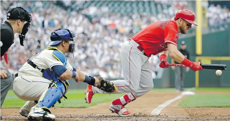  ?? — PHOTOS: AP ?? Cliff Pennington of the Angels lays down a bunt in front of Mariners catcher Carlos Ruiz during Sunday’s game in Seattle. The Angels won 4-2 to sweep the series.