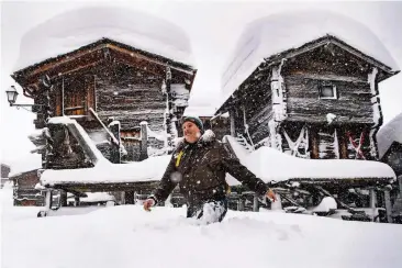  ??  ?? Ein Mann geht in Bellwald in der Schweiz an schneebede­ckten Hütten vorbei. In den vergangene­n Tagen hat es in Teilen der Schweiz und in Österreich massiv geschneit.