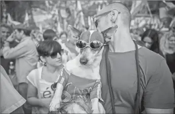  ?? AP PHOTO ?? A man carries a dog wearing the Spanish colours while people celebrate a holiday known as “Dia de la Hispanidad” or Spain’s National Day in Barcelona, Spain yesterday.