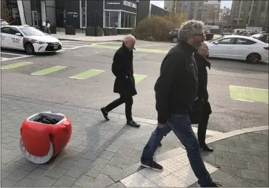  ?? MATT O’BRIEN — ASSOCIATED PRESS ?? Piaggio Fast Forward CEO Greg Lynn, front center, is followed by his company’s Gita carrier robot as he crosses a street in Boston. The two-wheeled machine is carrying a backpack and uses cameras and sensors to track its owner.