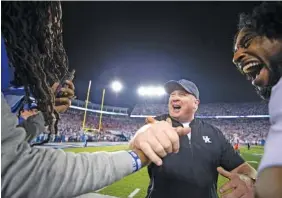  ?? AP PHOTO/MICHAEL CHUBB ?? Kentucky football coach Mark Stoops, center, slaps hands with rapper Waka Flocka Flame, left, after the Wildcats beat Florida on Oct. 2 in Lexington, Ky.