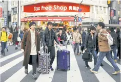  ??  ?? Travellers and local residents cross a street outside a duty-free department store popular among Chinese tourists in Tokyo.