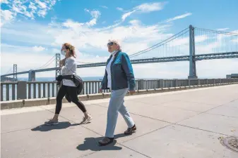  ?? Photos by Nick Otto / Special to The Chronicle ?? Two people stroll along the Embarcader­o in San Francisco — one wears a mask, the other not.