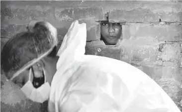  ?? RAJESH KUMAR SINGH/AP ?? A girl peers through a hole in the wall of her home as a health care worker prepares to test villagers for the virus in Uttar Pradesh, India. Just 5% of India’s 1.4 billion people are fully vaccinated, while about 20% have had a first dose.