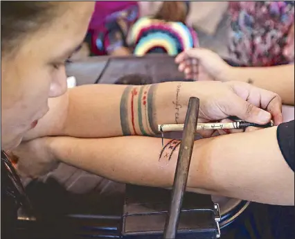  ?? ?? An apprentice of Apo Whang-Od tattoos a client at the Coffee and Ink, Atbp. weekend fair in Rizal Park’s Noli Me Tangere Garden yesterday. The batok sessions, organized by the Urban Arts & Crafts Fair, are being offered on Fridays, Saturdays and Sundays in March.