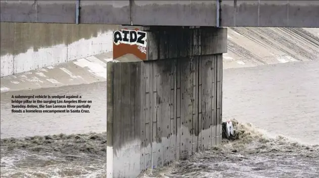  ?? ?? A submerged vehicle is wedged against a bridge pillar in the surging Los Angeles River on Tuesday. Below, the San Lorenzo River partially floods a homeless encampment in Santa Cruz.