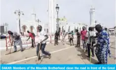  ?? AFP ?? DAKAR: Members of the Mouride Brotherhoo­d clean the road in front of the Great Mosque of the Mourides yesterday before its inaugurati­on. —