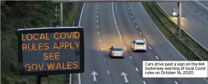  ??  ?? Cars drive past a sign on the M4 motorway warning of local Covid rules on October 16, 2020