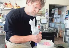  ??  ?? Jack Phillips decorates a cake at his store in Lakewood, Colo. He has stopped making wedding cakes and has lost about 40% of his business. BRENNAN LINSLEY/AP