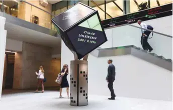  ??  ?? Visitors walk past an illuminate­d rotating cube displaying share price informatio­n at the London Stock Exchange (file). The FTSE 100 closed up 0.7% to 7,676.28 points yesterday.