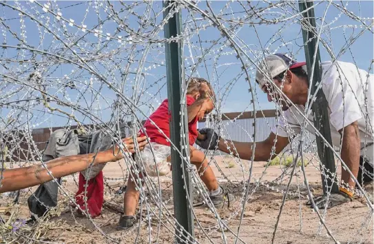  ?? Michael Robinson Chávez / The Washington Post ?? Venezuelan migrants negotiate razor wire as they cross the Rio Grande along the border wall between the United States and Mexico on Sept. 21 in Ciudad Juárez, Mexico. New York Mayor Eric Adams, a Democrat, is suing 17 charter bus companies for their role in an effort by Gov. Greg Abbott, R-texas, to send an estimated 30,000 migrants to the city.