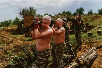  ?? David Goldman / Associated Press ?? Members of a Ukrainian unit carry logs Friday to fortify their position near Sloviansk in the eastern Donetsk region. Russian forces are expected to try to seize the fiercely contested area.