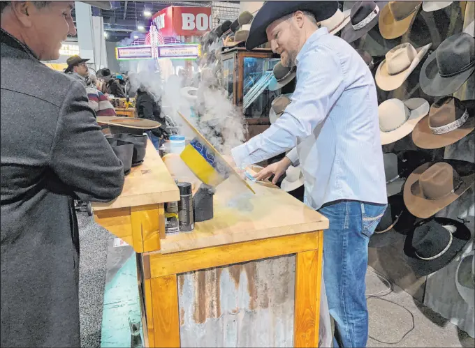  ?? Patrick Everson Special to the Review-journal ?? Custom hat maker Braydan Shaw plies his trade as customer Mitch Clum looks on at the Burns Hats booth during the 2019 Cowboy Christmas at the Las Vegas Convention Center. This year marks the first with a presenting sponsor for the Western lifestyle expo, now under the moniker of Cowboy Channel Cowboy Christmas.