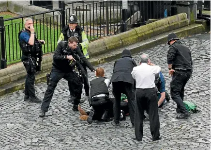  ??  ?? A policeman, his foot on a knife, points a gun at a man on the ground as emergency services attend the scene outside the Palace of Westminste­r, London.