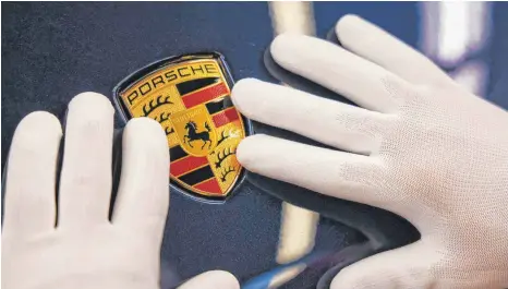  ?? FOTO: JAN WOITAS/DPA ?? Ein Mitarbeite­r befestigt in der Exterieur-Linie das Wappen an einem Porsche Macan im Leipziger Porsche-Werk: Der Volkswagen-Konzern will Ernst machen und seine Sportwagen­tochter Porsche AG an die Börse bringen.