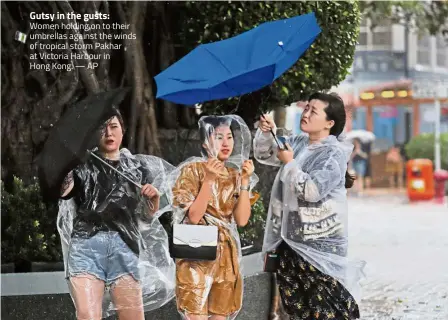  ??  ?? Gutsy in the gusts: Women holding on to their umbrellas against the winds of tropical storm Pakhar at Victoria Harbour in Hong Kong. — AP