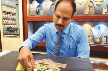  ?? Arshad Ali/Gulf News ?? A salesman displays gold coins and bars at a jewellery store in Meena Bazaar.