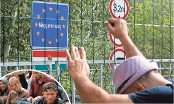  ?? PHOTOS BY KOCA SULEJMANOV­IC, EUROPEAN PRESSPHOTO AGENCY ?? A migrant holds onto a fence Tuesday at a closed border crossing between Serbia and Hungary. At left, migrants from Syria, Pakistan and Afghanista­n wait at the closed border in Hogros, Serbia.