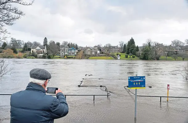  ??  ?? SUBMERGED: A man takes a photo of the viewing platform by the River Tay at the North Inch, Perth, which has been all but covered by flood water.