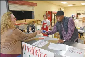  ?? STACI VANDAGRIFF/RIVER VALLEY & OZARK EDITION ?? Tarshawn Whitehead hands water to Carol Huffman of Lamar while helping out at the Mistletoe Market concession stand at the Dardanelle site of the Boys & Girls Club of the River Valley. Whitehead started in August as unit director of the club. CEO Megan Selman said he is a great role model for the students.