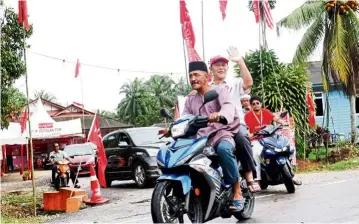  ??  ?? Campaign duty: Karmaine (waving) riding on a bike to meet voters at the villages near the teluk Kerang polling district centre in Pontian.