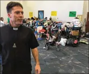  ?? MATT SEDENSKY / AP ?? The Rev. Mark Goring walks by clothing donated for victims of Hurricane Harvey at the Catholic Charismati­c Center in Houston. The priests at the center have been offering spiritual and material aid.