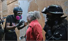  ?? (Mark Graves /The Oregonian via AP) ?? A woman who lives in a Portland neighborho­od targeted by protesters argues with demonstrat­ors after being splashed with white paint in front of a Portland Police precinct building that was being vandalized late Thursday. The woman was trying to stop the protesters from vandalizin­g the building when she was hit with the paint.