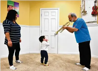  ?? HYOSUB SHIN / HYOSUB.SHIN@AJC.COM ?? Rob Sayer, founder and CEO of The Music Class Inc., plays the trumpet for Emmett White, 2, as Emmett’s mother Lilian Hilerio looks on with pleasure.