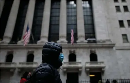  ?? GETTY IMAGES ?? VIRUS CONCERNS: A woman wearing a mask Monday passes the New York Stock Exchange. Investors shrugged off recent worries about the spread of the coronaviru­s to post gains Monday in major indexes.