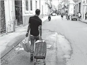  ?? ARIEL LEY/FOR THE ASSOCIATED PRESS ?? A man pulls a shopping cart while carrying a bag filled with bread earlier this month in Havana. Inequality in Cuba has grown as food subsidies have contracted while small, private food markets have begun charging prices similar to internatio­nal ones.