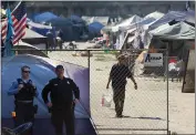  ?? SHMUEL THALER — SANTA CRUZ SENTINEL FILE ?? A resident of the Benchlands camp, at right, goes about his business as a police officer and a Santa Cruz Police Department community service officer monitor activity at the northern end of the encampment in September.