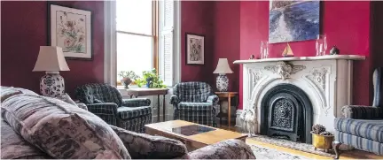  ??  ?? The walls in the living room and the dining room are painted tomato red. They form a striking contrast to the wainscotti­ng and the white trim around the windows and doors. The furnishing­s are homey with more formal antique pieces scattered here and...