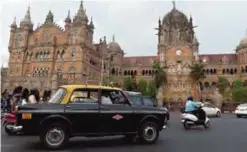  ??  ?? An Indian taxi driver drives his Premiere Padmini past the iconic UN Heritage building Chattrapat­i Shivaji Terminus railway station in Mumbai.