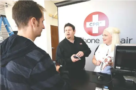  ?? STAFF PHOTO BY TIM BARBER ?? Ryan Cook, center, and Kalyn Cook talk to Nathan Dodd about the benefits of a cell phone accessory Wednesday at CPR Cell Phone Repair on North Market Street.