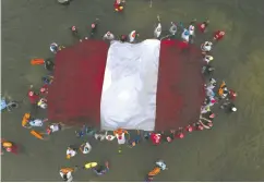  ?? GUADALUPE PARDO / AP PHOTO FILES ?? Swimmers, paddlers and surfers form a circle around a
Peruvian national flag as a show for unity and peace.