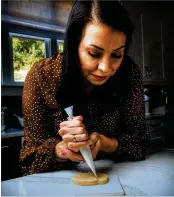  ?? ?? Using her icing bag tool as a sort of paintbrush, Sam Opdenbosch works on one of her cookie creations in her home kitchen in Marietta.