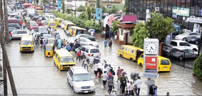  ??  ?? Pedestrian­s and motorists battling flooding after a rain shower in Lagos