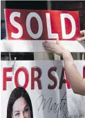  ??  ?? A real estate agent puts up a “sold” sign in front of a house in Toronto.