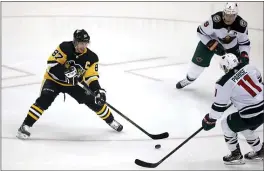  ?? GENE J. PUSKAR — THE ASSOCIATED PRESS ?? Pittsburgh’s Sidney Crosby, right, gets off a pass with Minnesota’s Zach Parise (11) and Mikko Koivu (9) defending during the first period Tuesday. Crosby scored four points in his first game since undergoing abdominal surgery Nov. 14. The Penguins won, 7-3.