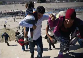  ?? AP PHOTO/RAMON ESPINOSA ?? Migrants walk up a riverbank at the Mexico-U.S. border after getting past a line of police at the Chaparral border crossing in Tijuana Sunday.