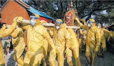  ?? NIRANJAN SHRESTHA/AP ?? Nepalese devotees in protective gear carry the chariot during a festival in Kathmandu, celebrated this year during the day because of the pandemic.